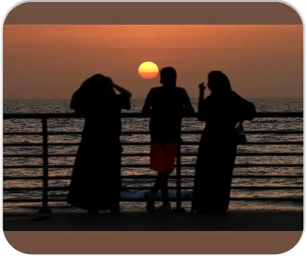People stand on the corniche at sunset in Jeddah