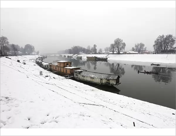 Moored houseboats are seen along the Jehlum river as Kashmiri fishermen row boats during