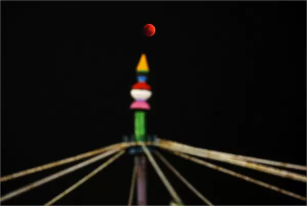A lunar eclipse of a full Blue Moon is seen rising over a roller coaster ride in
