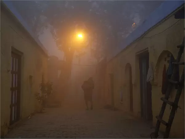 A man walks out of his house in an alley on a cold and foggy morning in New Delhi