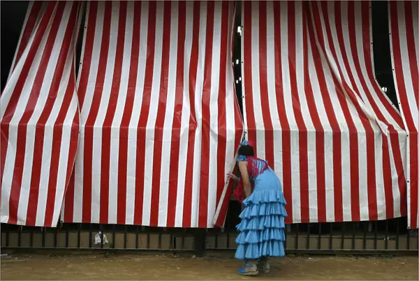 A woman wearing a traditional Sevillana dress looks into a stall at a fair in Seville