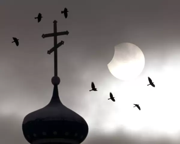 Birds fly past an Orthodox church during a partial solar eclipse in the town of Volozhin