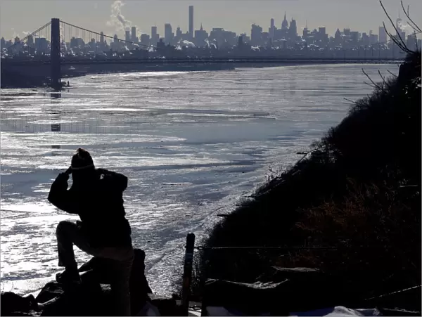 A woman photographs ice on the Hudson River, with the George Washington Bridge