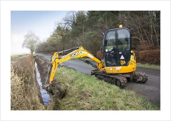 Cleaning out roadside drainage ditches which had become overgrown using JCB digger, England, February