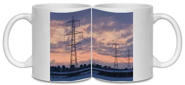 Electricity transmission pylons and overhead wires, crossing over snow covered farmland at sunset, Dorset, England