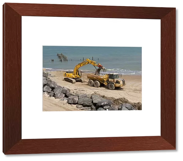 Excavator and truck on beach, repairing sea defences with boulders, Happisburgh, Norfolk, England, august