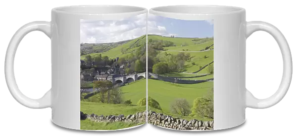 View of five arched stone bridge over River Wharfe, drystone wall, pasture, trees and village, Burnsall, Wharfedale