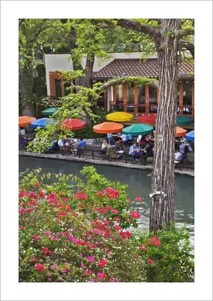 Tourists dining in outdoor cafe under colorful umbrellas on the famous River Walk