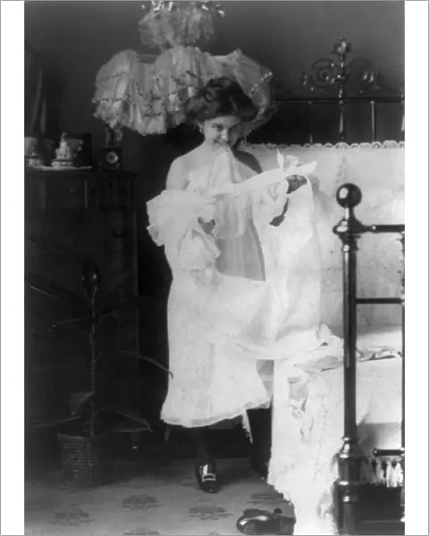 WOMAN: NIGHTGOWN, c1900. A woman putting on a nightgown before going to bed. Photograph
