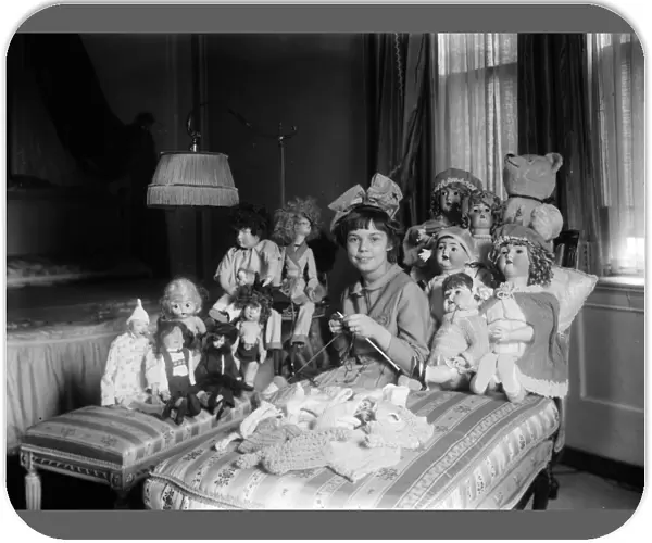 GIRL AND DOLLS, c1910. A young girl knitting doll clothes