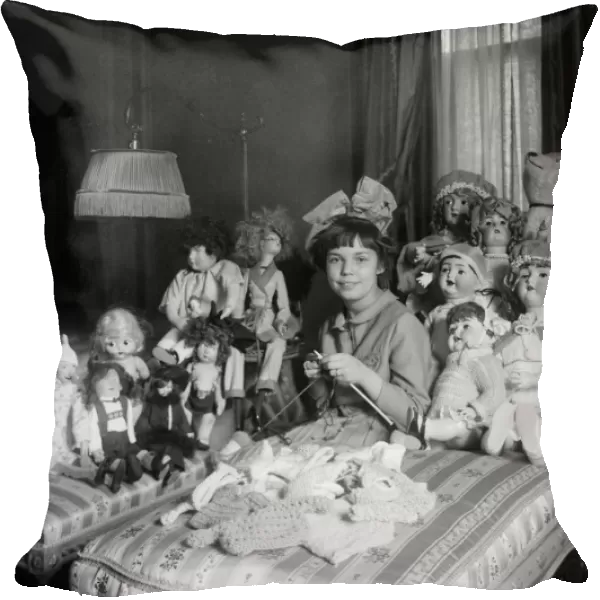 GIRL AND DOLLS, c1910. A young girl knitting doll clothes