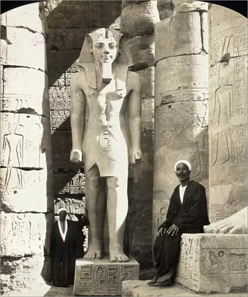 EGYPT: LUXOR TEMPLE. A man seated next to a statue of Ramesses II at the Luxor Temple