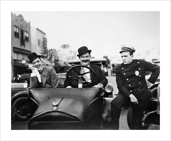 LAUREL AND HARDY, 1928. Stan Laurel, left, and Oliver Hardy with a police officer in the silent film Leave Them Laughing, 1928