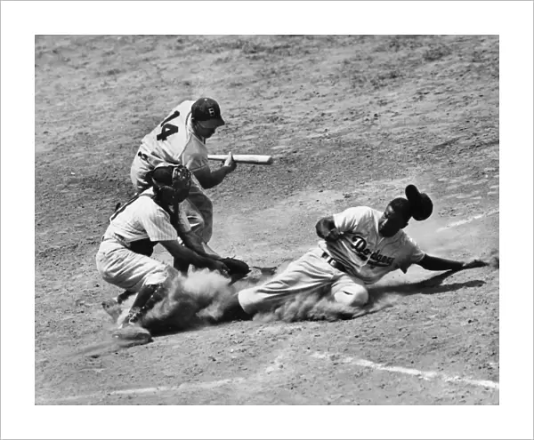 JACKIE ROBINSON (1919-1972). John Roosevelt Robinson, known as Jackie. American baseball player. As a member of the Brooklyn Dodgers, stealing home under the tag of catcher Andy Seminick in a game against the Philadelphia Phillies, at Shibe Park, Philadelphia, Pennsylvania, 2 July 1950. The Dodgers batter is Gil Hodges