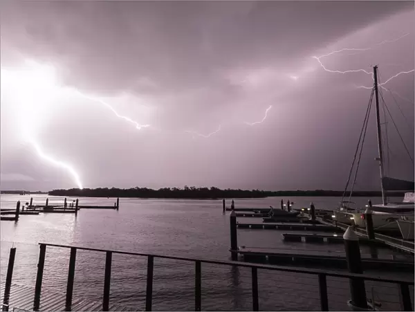 Flashes of bright lightning strikes across the water with boats silhouetted