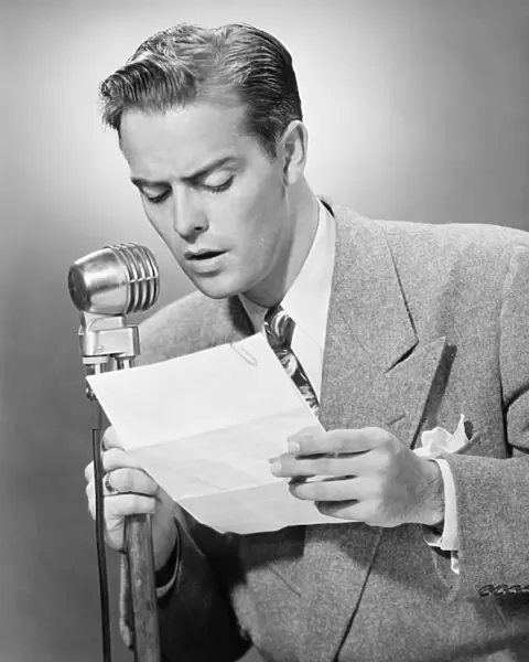 Elegant man talking into microphone in studio, (B&W)