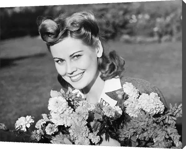 Woman in yard holding bunch of flowers, (B&W), portrait