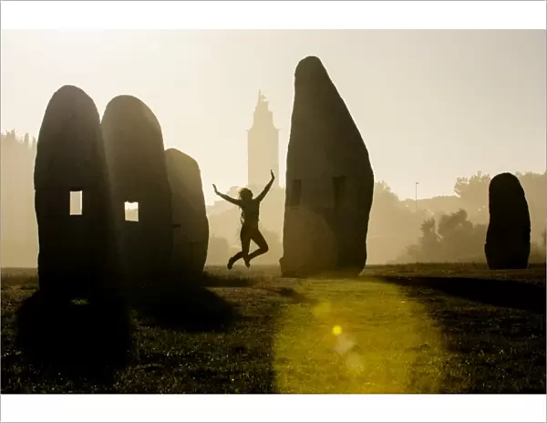 Young woman jumping in midair outdoors, in front of Hercules Tower, A Coruna, Spain