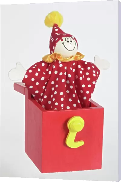 Jack in a box, smiling clown puppet popping out of red wooden box with arms extended to sides, front view