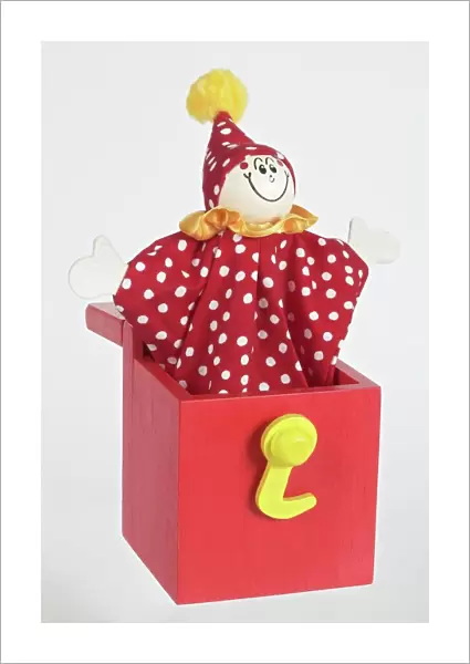Jack in a box, smiling clown puppet popping out of red wooden box with arms extended to sides, front view