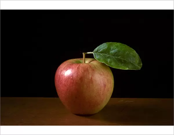Apple with leaf on wooden surface against black background credit: Marie-Louise