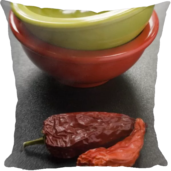 Two bright melamine bowls stacked on dark surface with two red hot chilli peppers