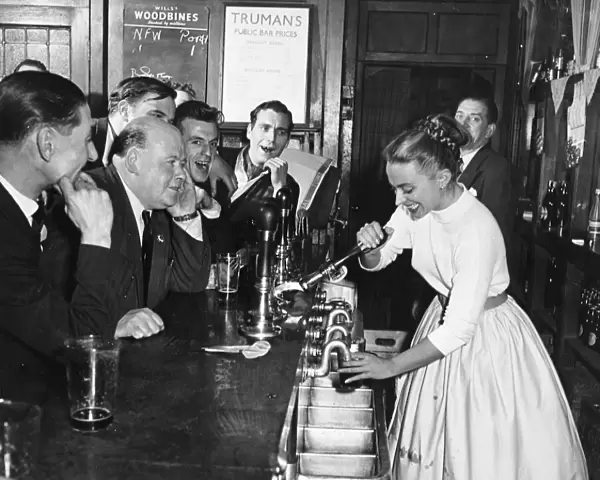A woman barmaid pulls a pint of beer for male customers in a London pub, England. 1950s