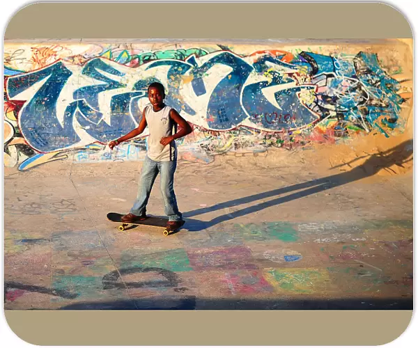 A young boy skateboards past a ramp decorated with graffiti in a skate park in Durban