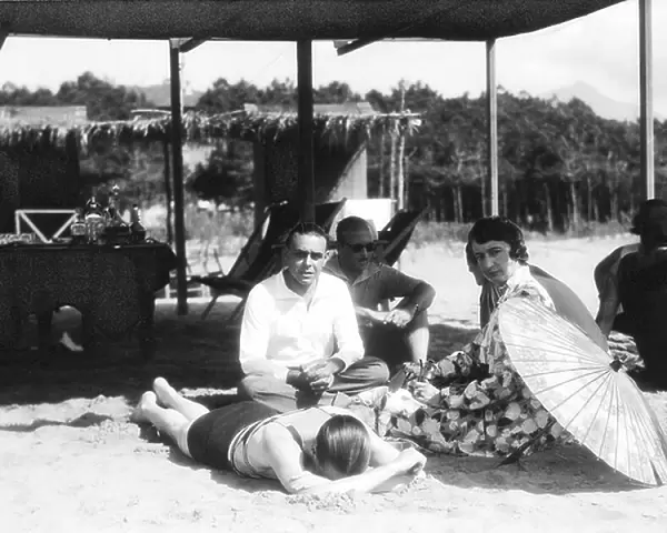 Portrait of a group of people seated on the beach, under a parasol shed roof. In the background a wood can be glimpsed, Versilia