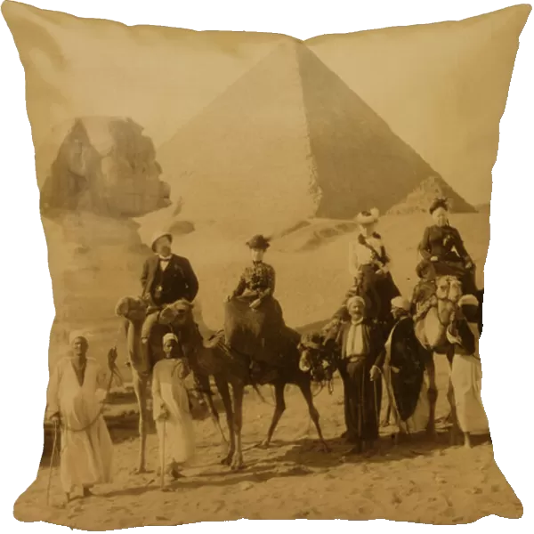 Three women and a man in western attire, seated on camels, several local men stand before the camels holding the reins, a pyramid and the sphinx in background 1880 (photo)