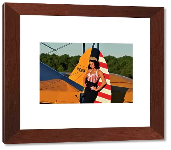 1940s style pin-up girl leaning on the tail fin of a Stearman biplane