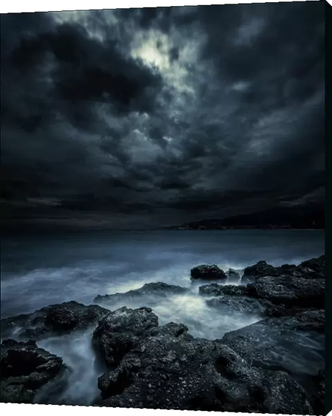 Black rocks protruding through rough seas with stormy clouds, Crete, Greece