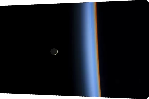 View of a crescent moon rising and the cusp of Earths atmosphere