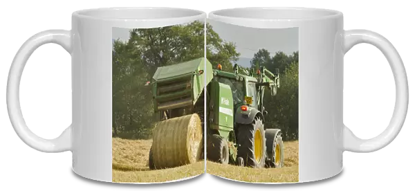 Baling machine ejecting a bale of Barley straw on arable farmland, Scotland, UK