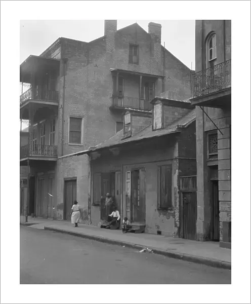 View from across street of a man and child sitting on steps and a woman walking down... c1920-1926. Creator: Arnold Genthe