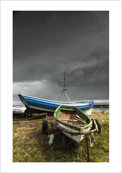 Rowboats sitting on trailers on the shore under storm clouds; Boulmer northumberland england