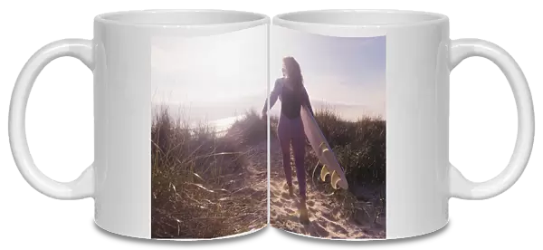 A woman carries her surfboard down a sandy path to the beach; Tarifa cadiz andaulsia spain
