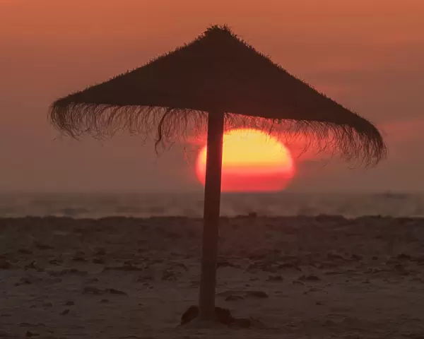 Silhouette Of A Beach Umbrella On The Beach With A Colourful Sun Sinking Into The Horizon Over The Ocean; Tarifa, Cadiz, Andalusia, Spain