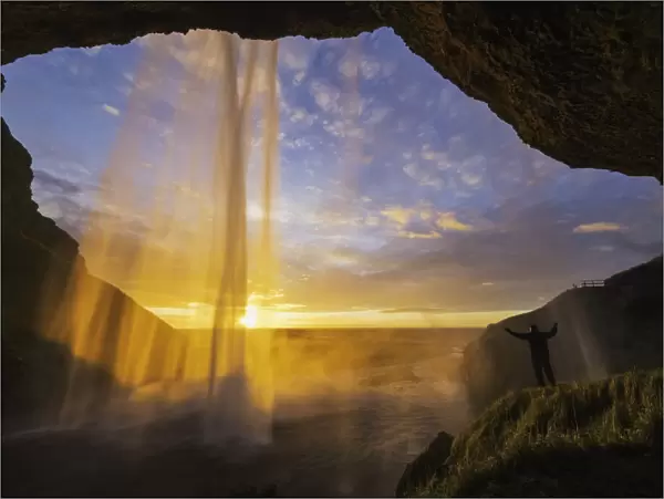 Man Standing Behind The Waterfall Known As Seljandafoss Along The Southern Coast Of Iceland; Iceland