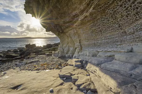 Close-up of rock face of sea cliff with honeycomb weathering and sun shining over Loch Scavaig on the Isle of Skye in Scotland, United Kingdom