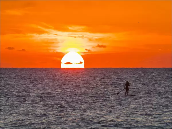 Silhouette of woman paddleboarding on Atlantic Ocean off the coast of Florida at sunrise, USA