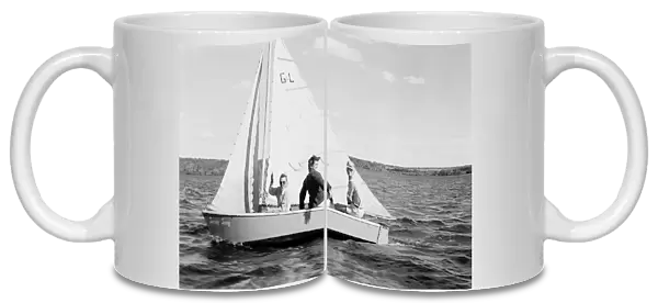 Historical image of three people sailing on Baptiste Lake in a sailboat, the woman waving at the camera, circa 1940; Athabasca County, Alberta, Canada
