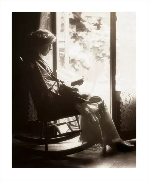 Woman in a rocking chair in front of the window, circa 1900