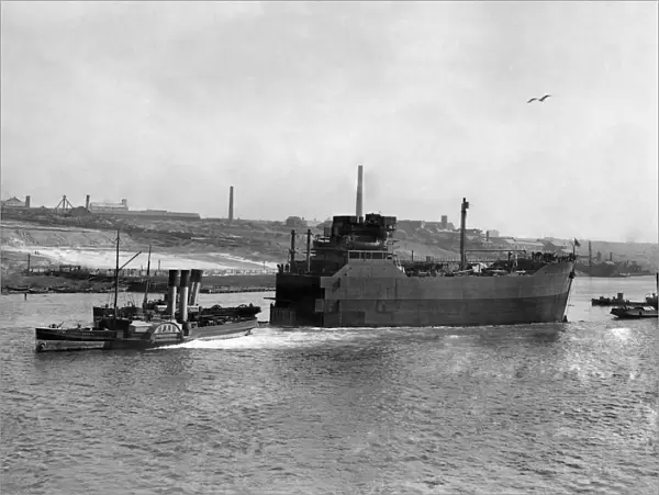 World War II Shipbuilding. Tugs pull The bow Section of a new cargo ship along the river