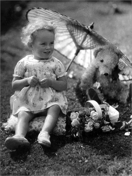 Young girl sitting in her back garden shading her teddy bear from the sun underneatha