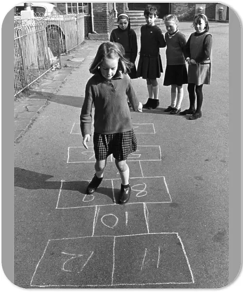 Young Pgirl playing a game oh hopscotch with her friends in the school playground