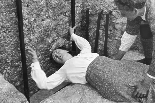 A women seen here with the aid of her gentleman friend kissing the Blarney stone at