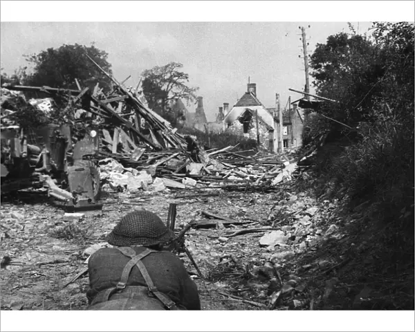 A Bren gunner takes up a position near wrecked houses on the roadway leading to