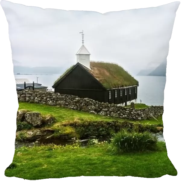 Summer view of traditional turf-top church in faroese village. Beauty landscape with foggy fjord and high mountains