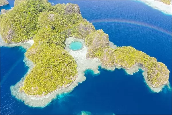 A rainbow appears above a rugged limestone island in Raja Ampat, Indonesia. This remote, tropical region is known for its marine biodiversity